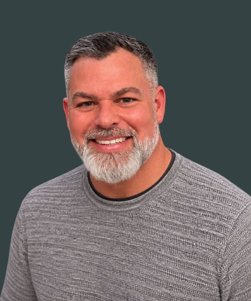 Portrait of Travis Judd, smiling, in casual gray sweater at The Rock Church USA.